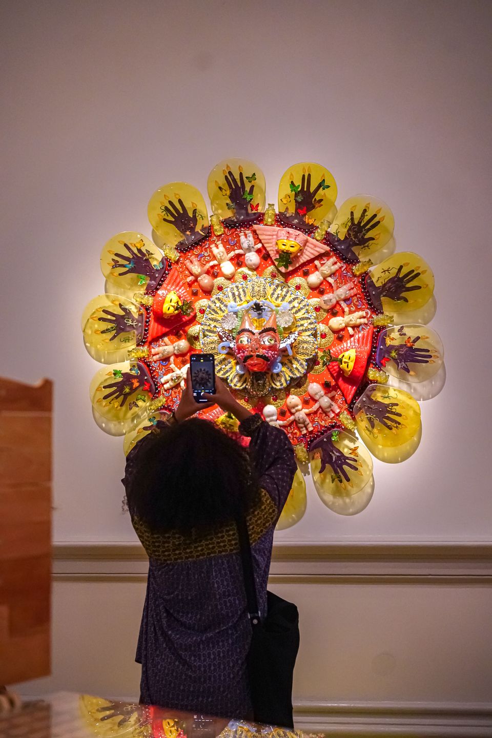 A visitor looks at a bright yellow, circular artwork and is taking a picture with a cell phone.