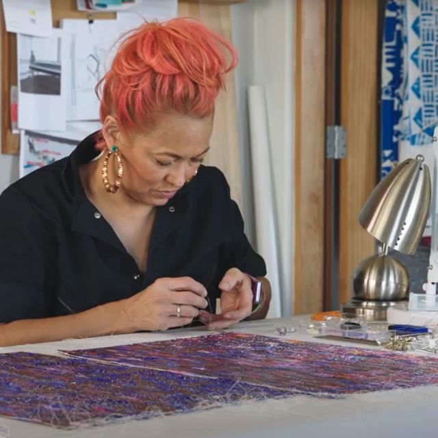 Artist Erica Lord sits at a table. She is beading.