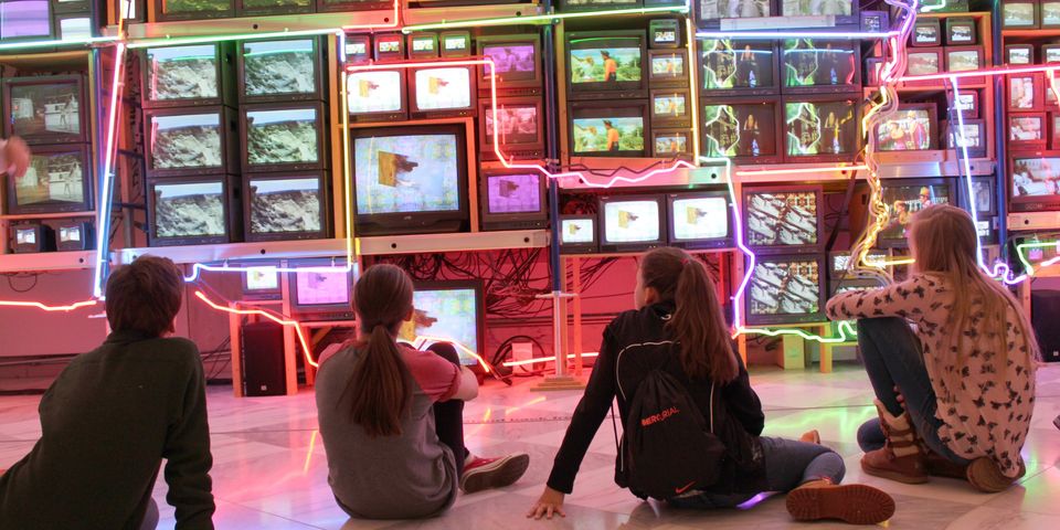 a group of children sit in from of a colorful neon artwork