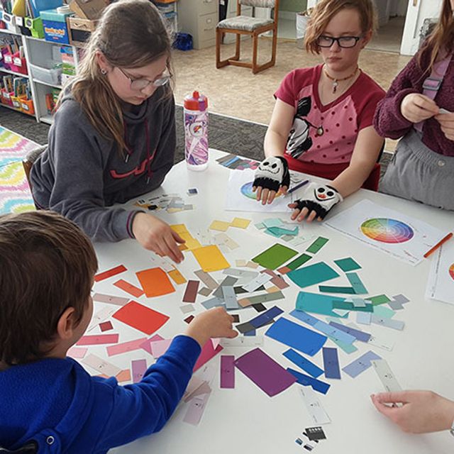 A group of students at a rural school sit around the table with colored trips assembling a color wheel.