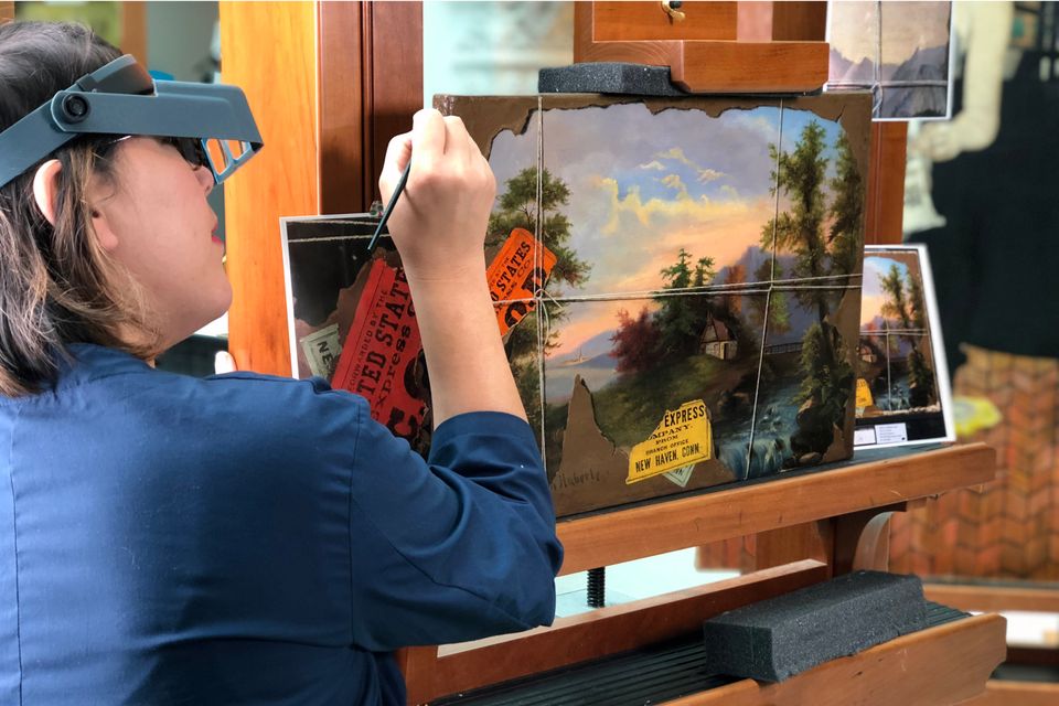 A conservator restores a painting with a paintbrush