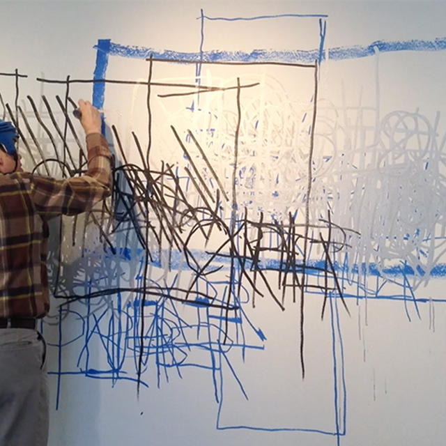 A man stands drawing on a white board.
