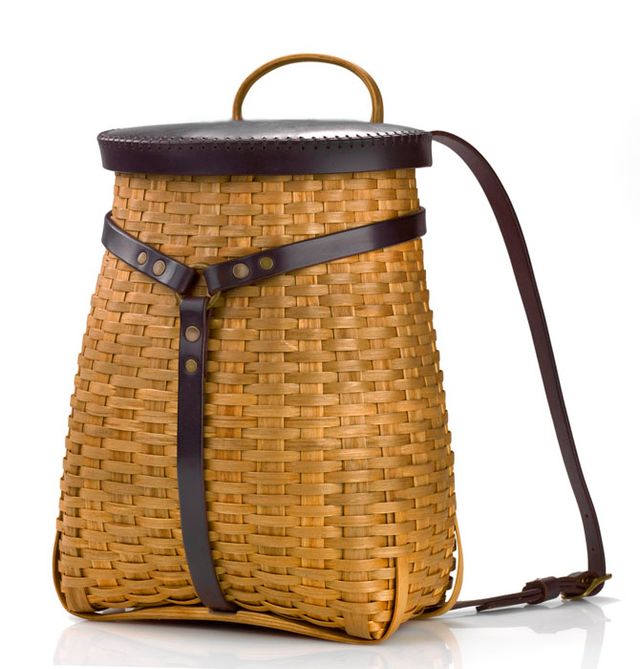 A tall basket with a rectangular bottom and a circular top with backpack straps made of leather.