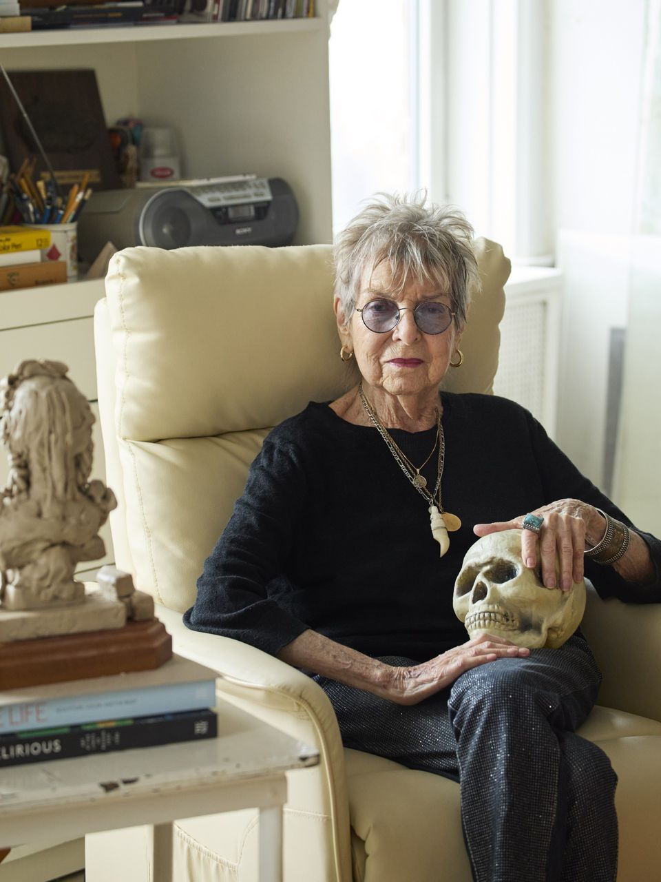 Photo of Audrey Flack sitting in a white chair holding a skull in her lap.