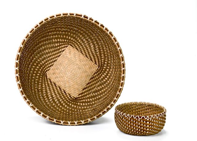 A large basket shaped like a large bowl and a small circular basket made with a spiral weave. The larger basket has a light square patch in its center.
