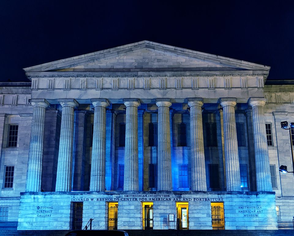 The Smithsonian American Art Museum facade at night with blue lights. 