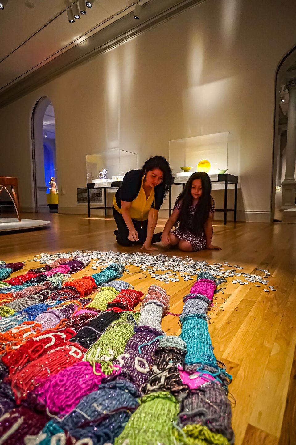 A woman and a child kneel in front of a large-scale knitted installation.