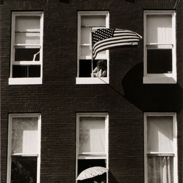 A black and white photograph of a two story home, a person is seen waving an American flag from the window