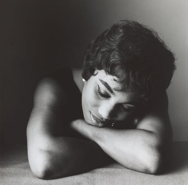 A photograph of a woman laying down with her hands folded and chin resting on her arms.
