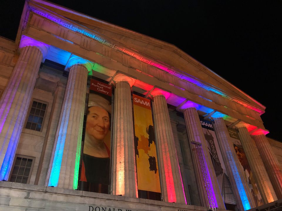 A photograph of the Smithsonian American Art Museum's exterior facade at night with rainbow lights.