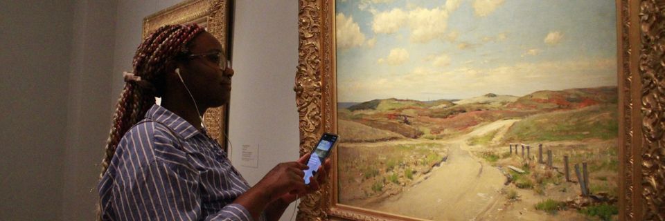 A woman stares at a painting while scanning it with ehr phone