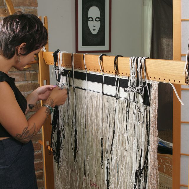 A woman with short hair works in front of a loom.