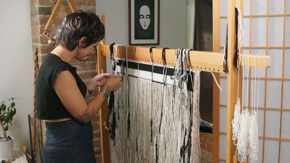 A woman with short hair works in front of a loom.