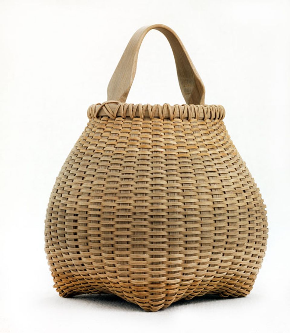 A basket that has a square base and flares out with a small circular top with a handle.