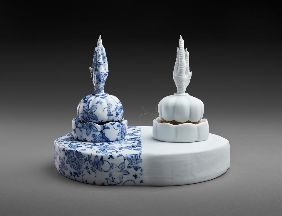 Two porcelain powderpuffs: one is all white and the other has blue painting; sculpted chicken feet are on the top of each powderpuff.