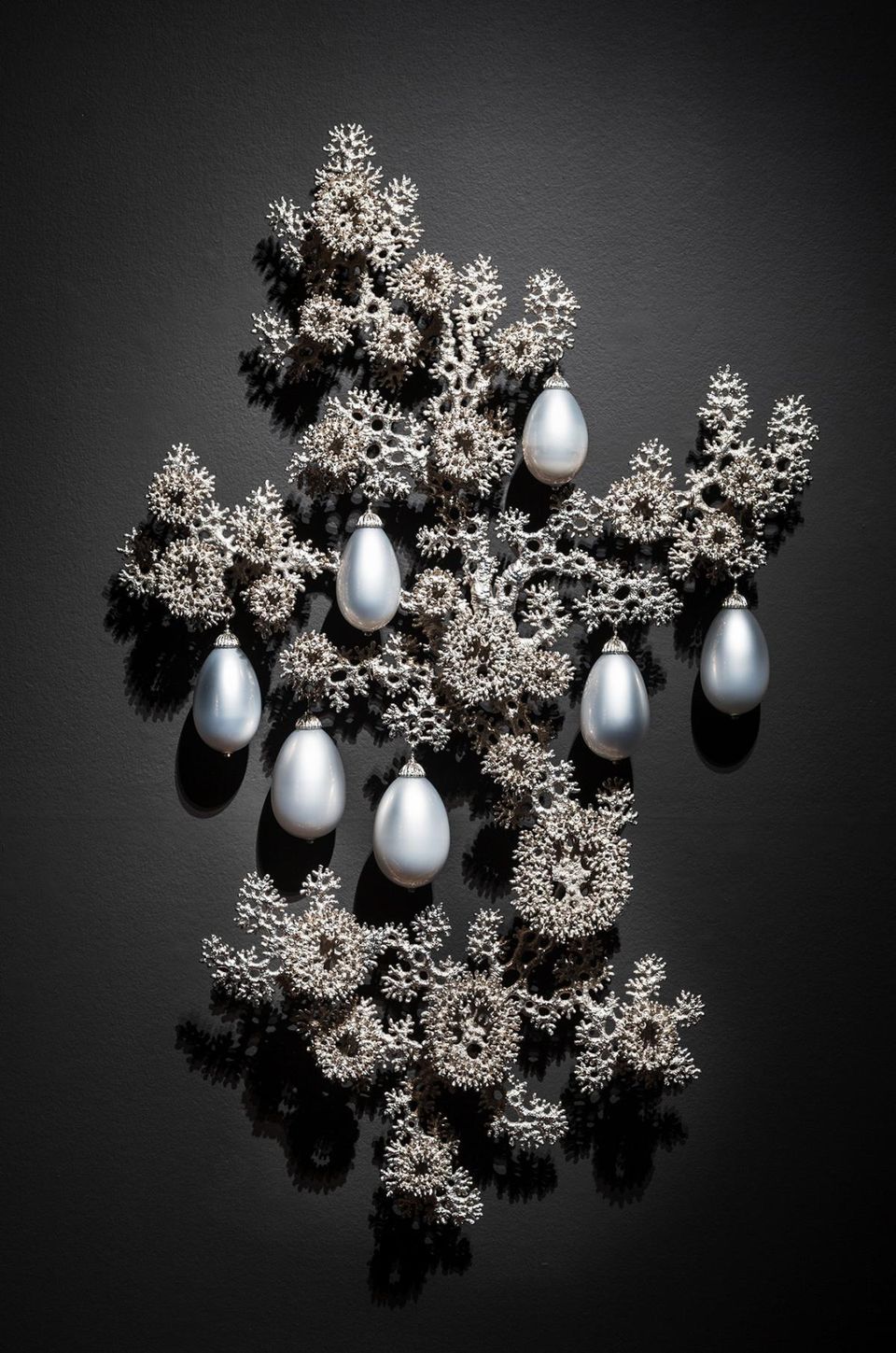 A photograph of a bronze and blown glass artwork with 7 silver balls hanging from a structure.