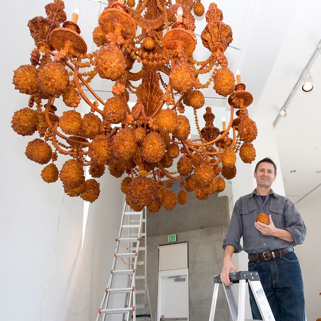 A photograph of an artist in a gallery with their work. 