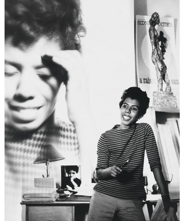 A photograph of a woman standing with an enlarged photograph behind her of herself. 
