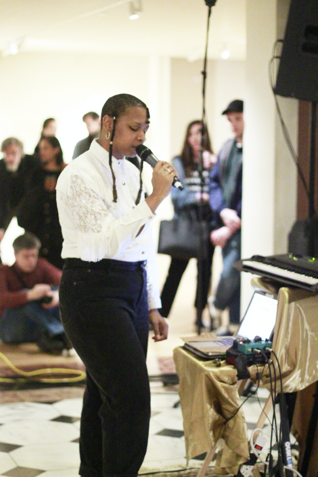 A musician wearing a white shirt and black pants sings into a microphone in the Luce Foundation Center.