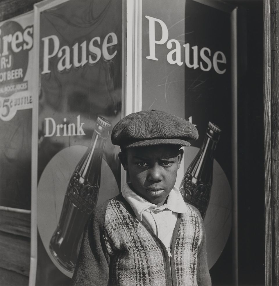 A photograph of a young boy standing next to a soda advertisement. 