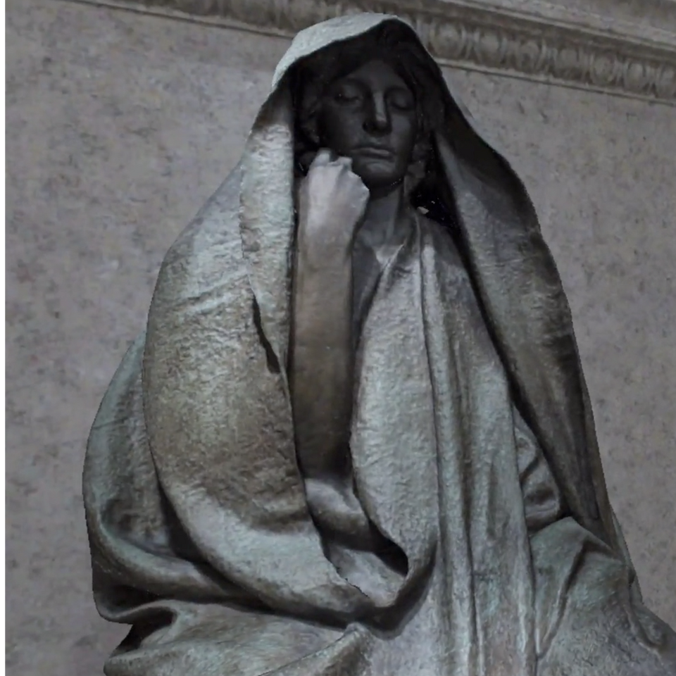 A sculpture of a woman sitting down with her hand on face and a cloth over her head.