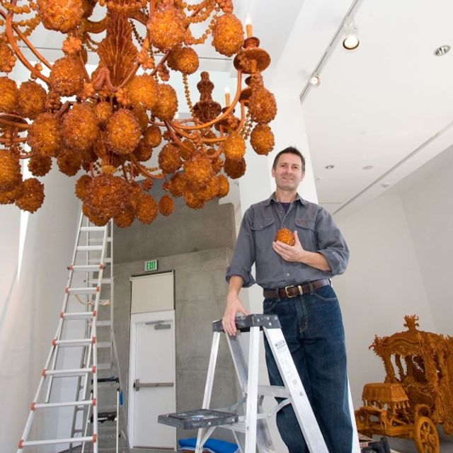 Artist Timothy Horn standing on ladder next to his large chandelier sculpture made of rock sugar