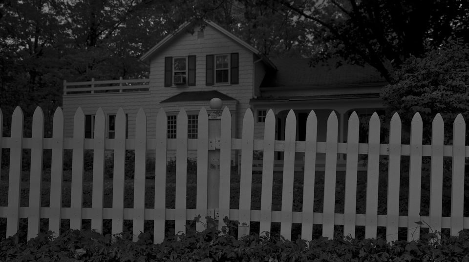 A photograph of a house with a white fence at night. 