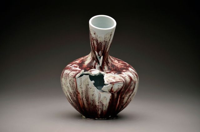 A photograph of a porcelain vase that has a hole in it and is leaning over. 