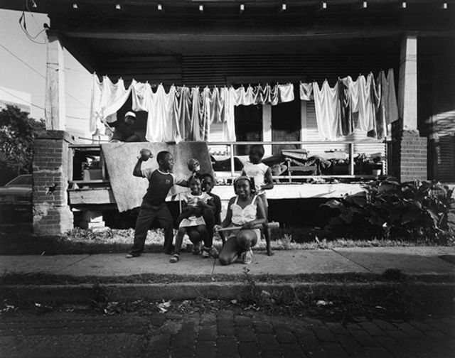 Hudnall's gelatin silver print of kids playing on the sidewalk in front of a house with drying laundry behind them.