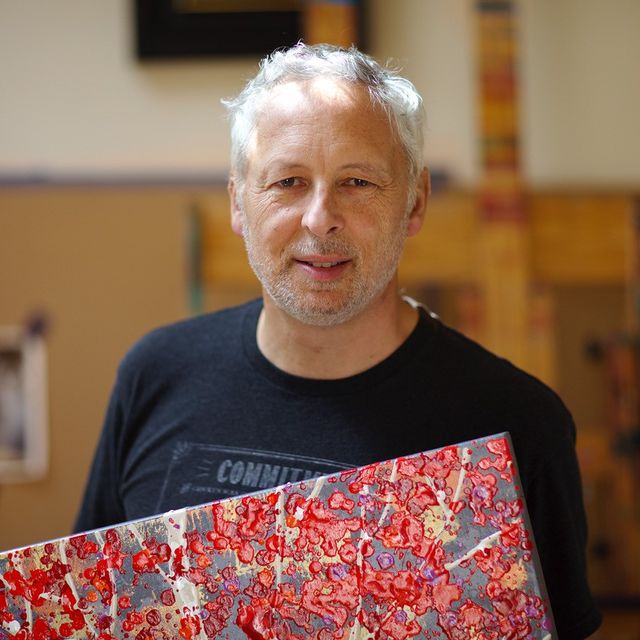 A photograph of a man holding a red painting. 