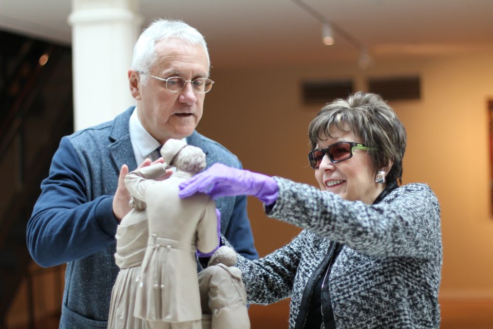A photograph taken inside the museum of a blind lady with gloves touching a replica of a sculpture.