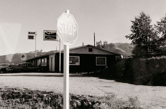 A photograph of a Colorado landscape with stop sign and building taken by automobile.