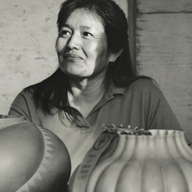 A black and white photograph of a woman sitting behind two ceramic pots