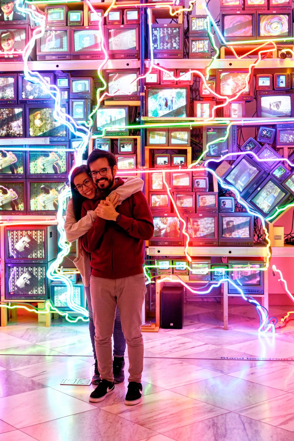 A couple hugs one another in front of a colorful sculpture 