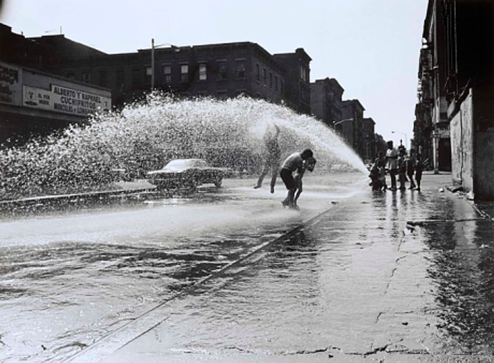 A photograph of children getting sprayed from a fire hydrant from the exhibition Down These Mean Streets: Community and Place in Urban Photography