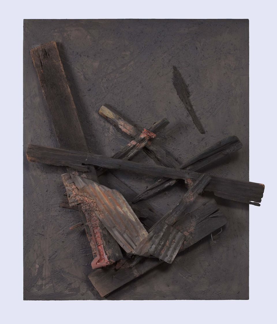 A square piece of dark brown wood is overlaid with wood pieces, metal, tin, and nails 