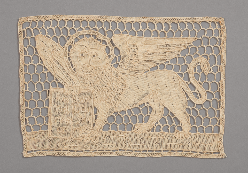 A rectangular piece of lace depicting a winged lion with a halo around its head holding a book, possibly the Bible.