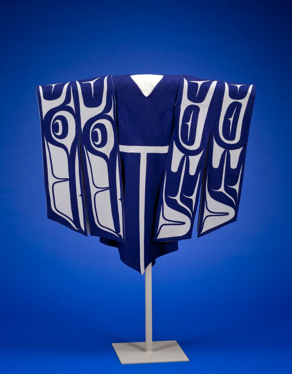 A blue dress handing on a stand with sleeves made of white and blue material depicting wings.