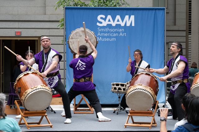 Japanese taiko drumming performers in front of a blue backdrop that says SAAM, Smithsonian American Art Museum.