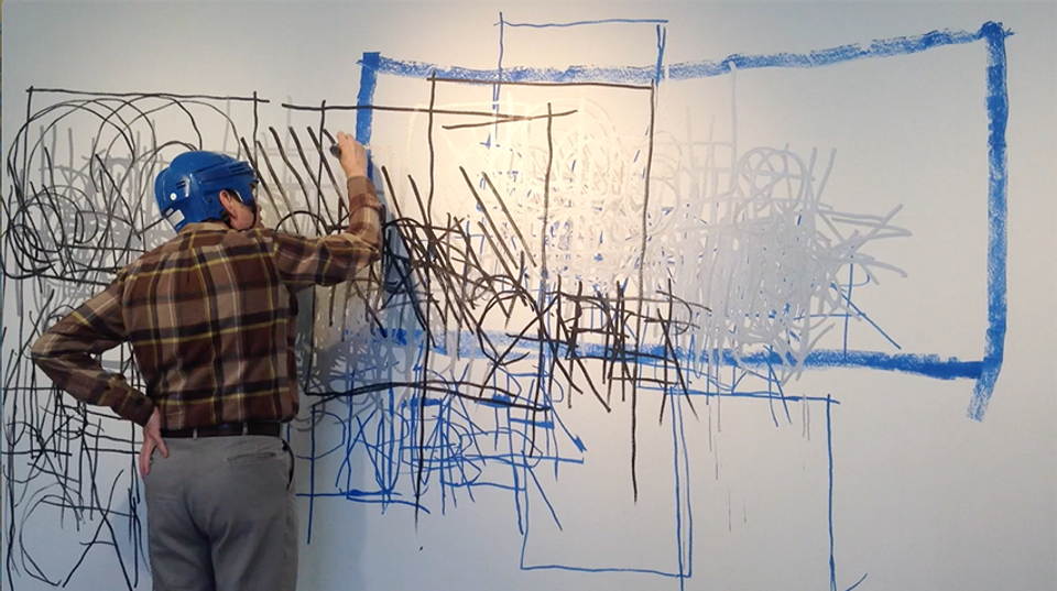 A man stands drawing on a white board.