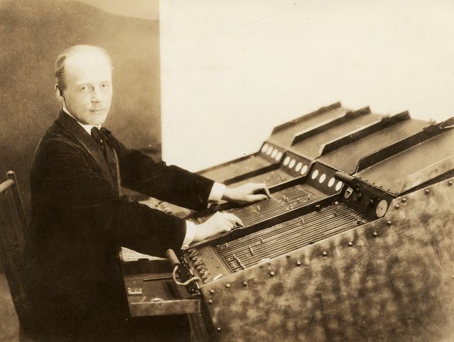 A sepia toned photograph of Thomas Wilfred sitting at a machine called a Clavilux, which he toured the country with creating art. 