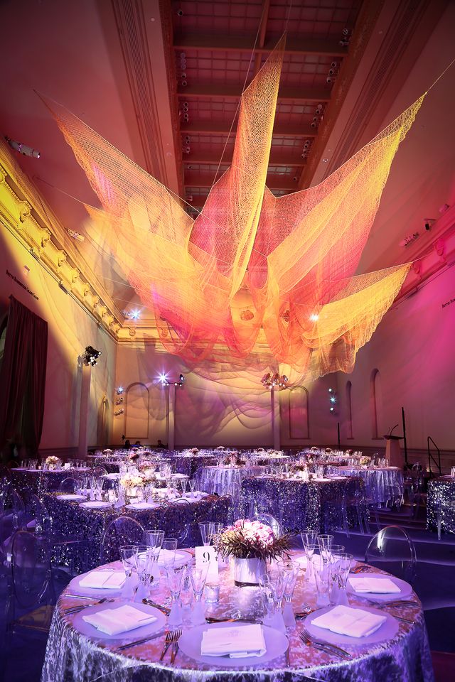 A photograph inside with tables set up and a colorful artwork hanging from the ceiling.