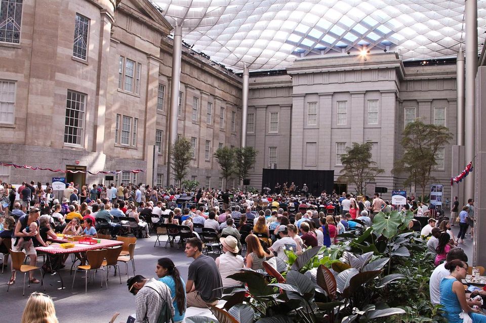 This image shows people gathered in the Kogod Courtyard for the America Now program listening to the band playing onstage