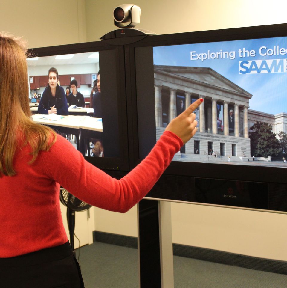 A photograph of a woman talking to a classroom remotely while also showing them a powerpoint on a split screen.