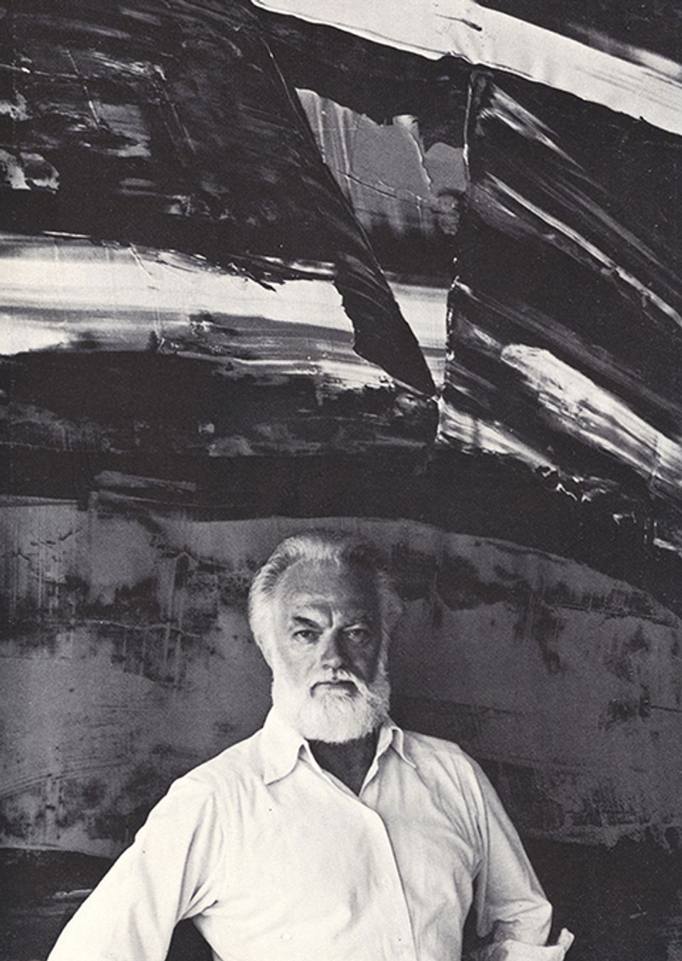 A photograph of a man standing in front of a painting. 