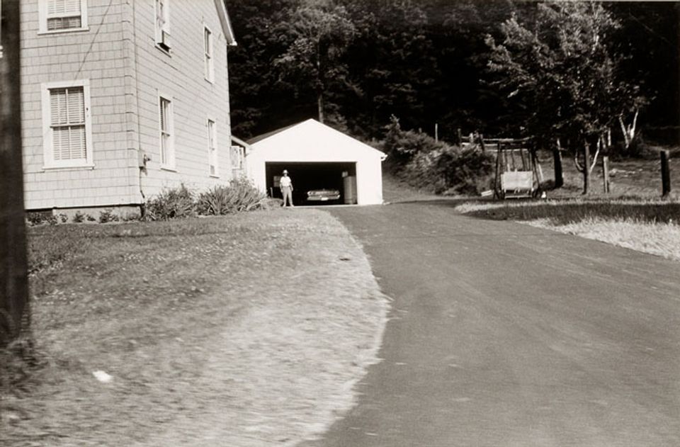 A photograph of a Massachusetts landscape with a house and driveway taken by automobile.