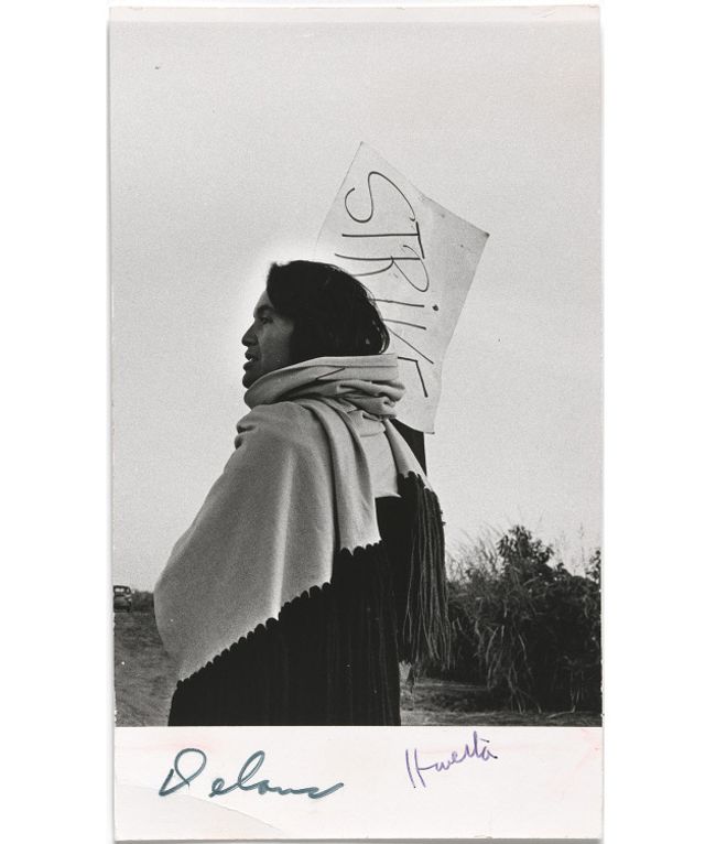 A photograph of a woman holding a protest sign with a scarf. 