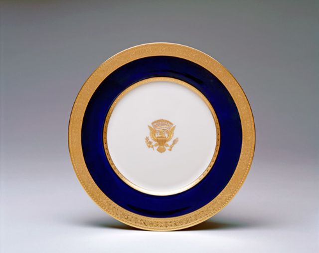 An image of a porcelain service plate with gold rim, blue outer circle and crest in the middle. 