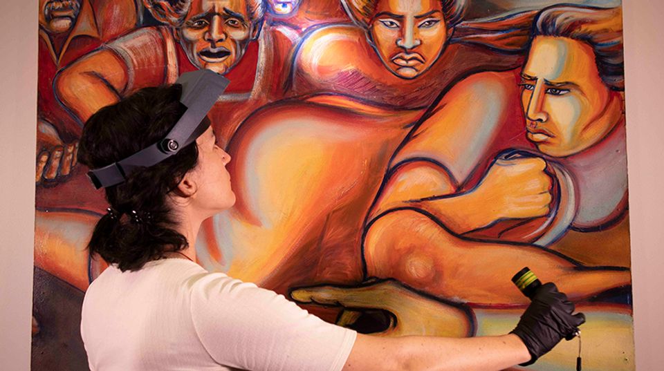 Conservator wearing a head lamp, shines light on a mural.