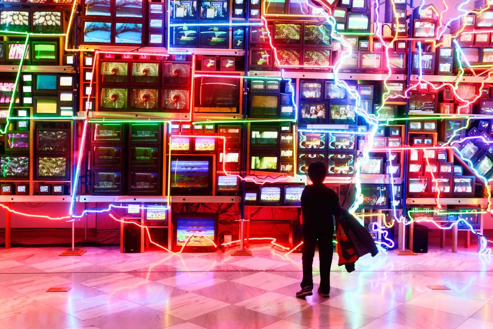 A small child stands in front of Nam June Paik's Electronic Superhighway